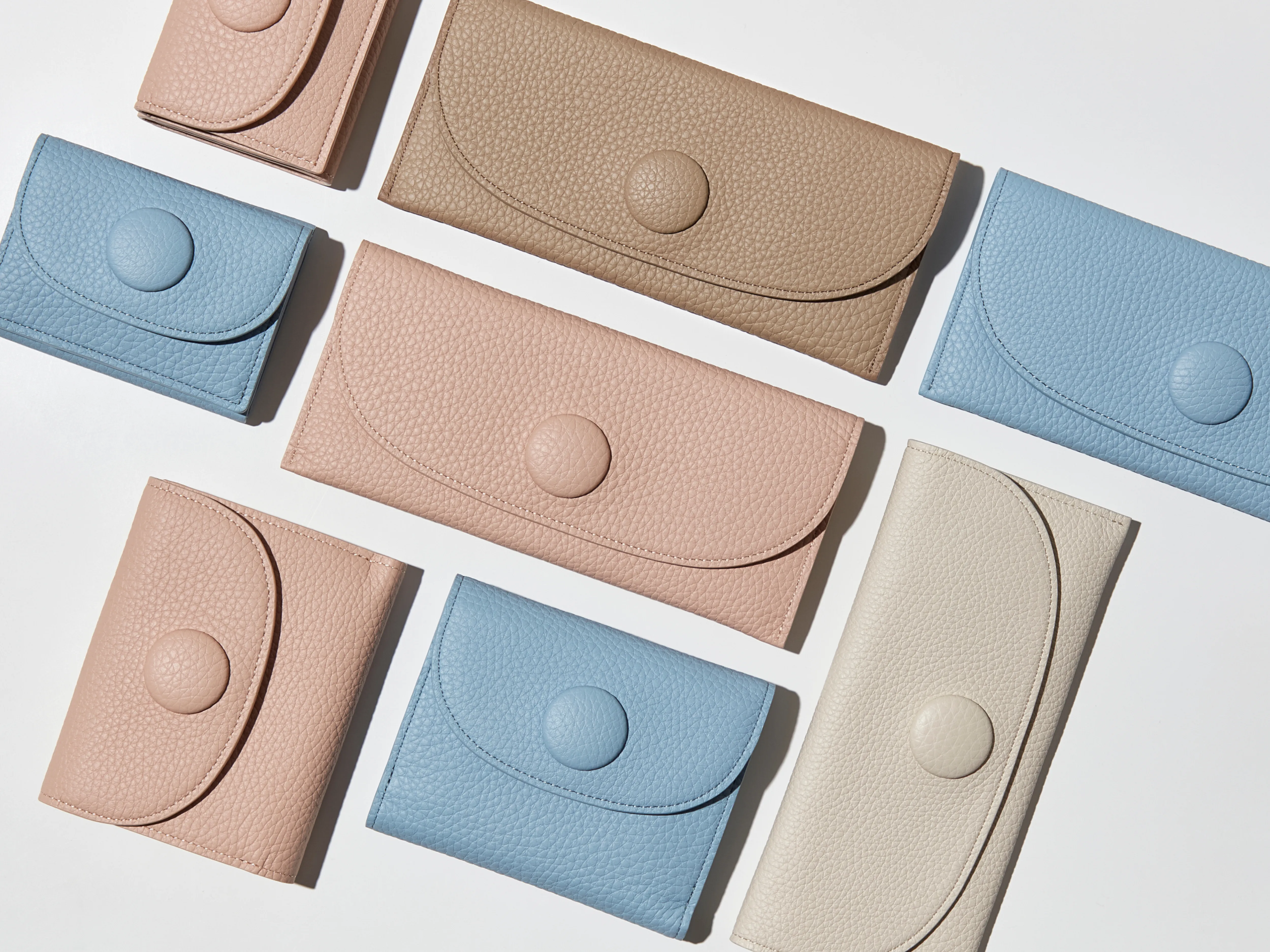 ピンクの折り財布と長財布、ブルーの折り財布と長財布、ベージュの長財布が並んでいる様子