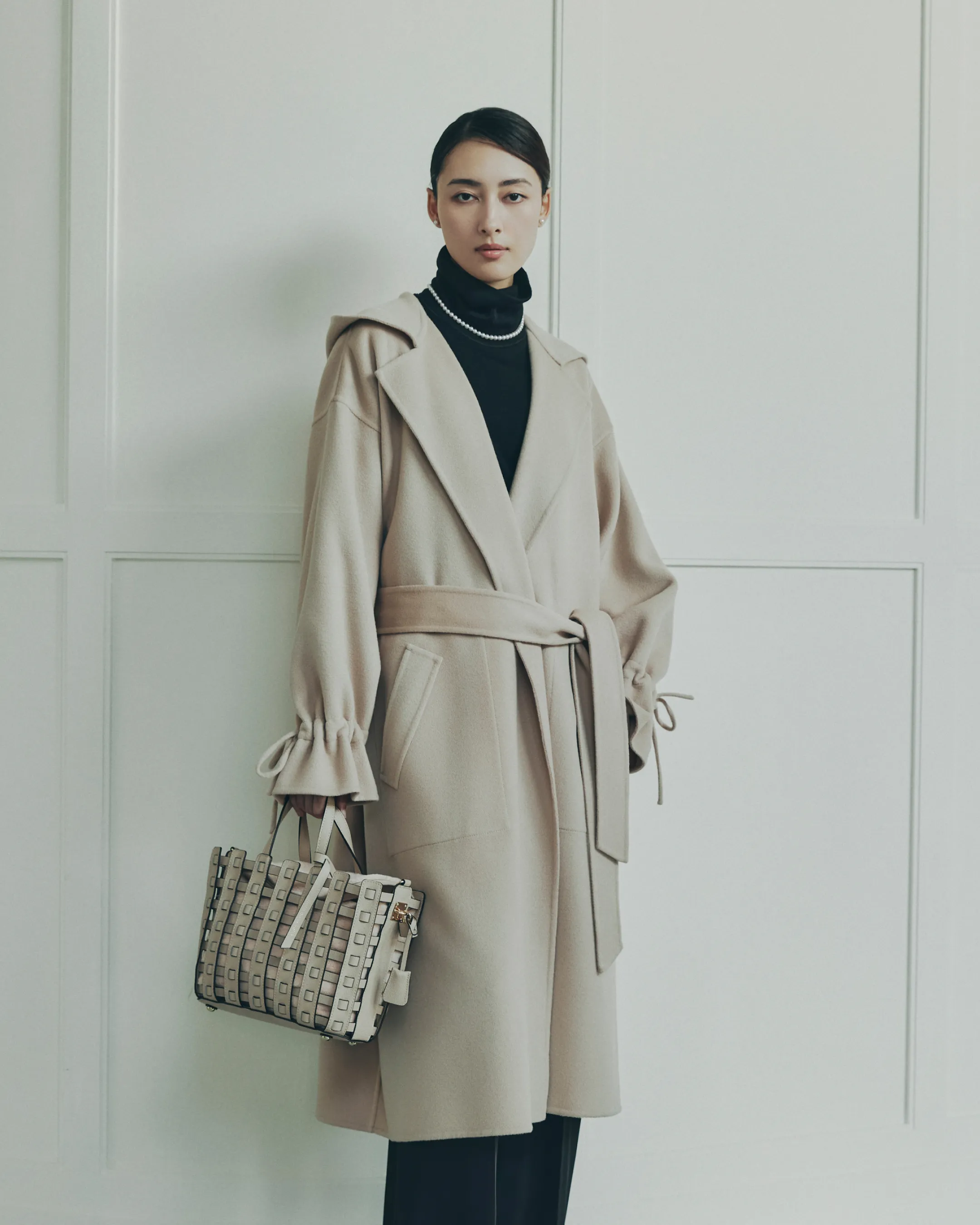 NEW CLOSET リバーフードコートをスカリオーネ タートルネックセーターに重ねて着用しているモデルがmica della valleメッシュトートバッグを持ち綺麗な姿勢で立っている様子