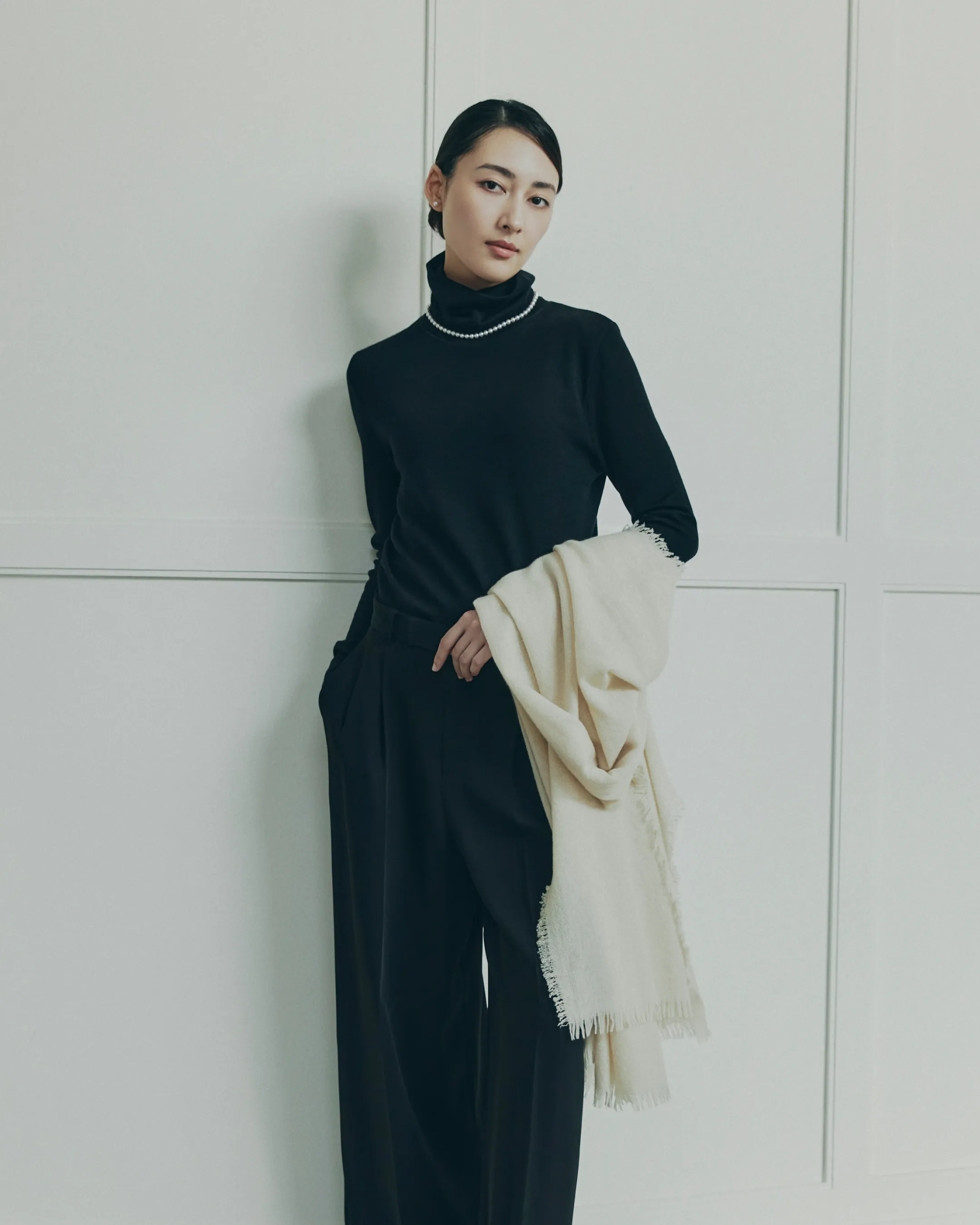 スカリオーネ タートルネックセーターを着用し、アソースメレ ストールを腕にかけるようにして持っているモデルが綺麗な姿勢で立っている様子