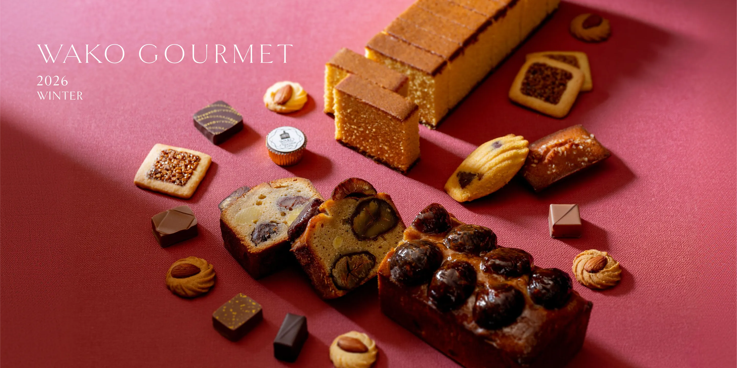 WAKO GOURMET 2026 WINTER。深いローズ色の布の上に、栗がのったパウンドケーキやかすてら、マドレーヌ、ナッツのクッキー、ショコラが並ぶ、冬の焼菓子とショコラの詰め合わせ