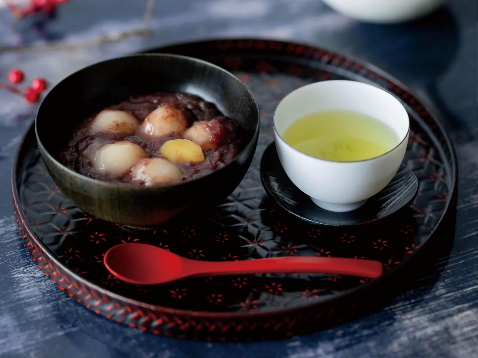 朱塗りの盆にのせた、白玉と栗が浮かぶ白玉ぜんざいと緑茶。赤い木の実が冬の趣を添える