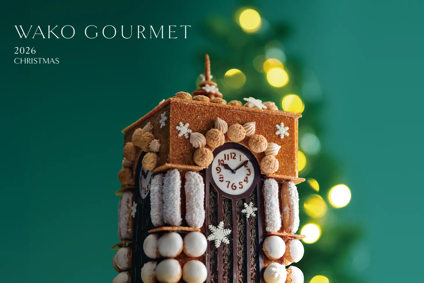 WAKO GOURMET 2026 CHRISTMAS。深い緑を背景にきらめくツリーの灯りの前に立つ、雪の結晶で飾られた和光の時計塔をかたどったクリスマスケーキ